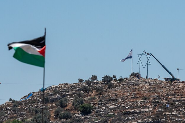 Palestine flag flying in West Bank with a metal Star of David and Israeli flag in the background